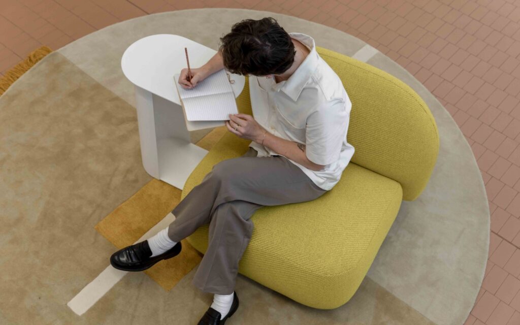 Design student sketching ideas in a notebook while seated in a yellow armchair