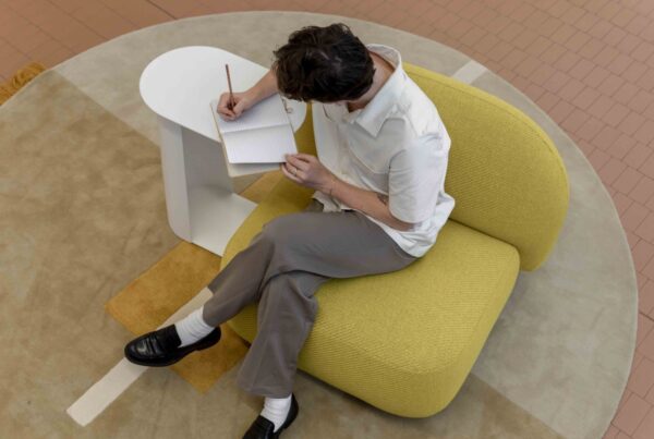 Design student sketching ideas in a notebook while seated in a yellow armchair